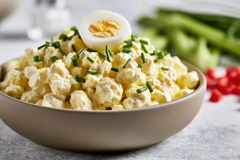 Classic egg salad in a matte taupe ceramic bowl topped with a halved hardboiled egg and chopped chives