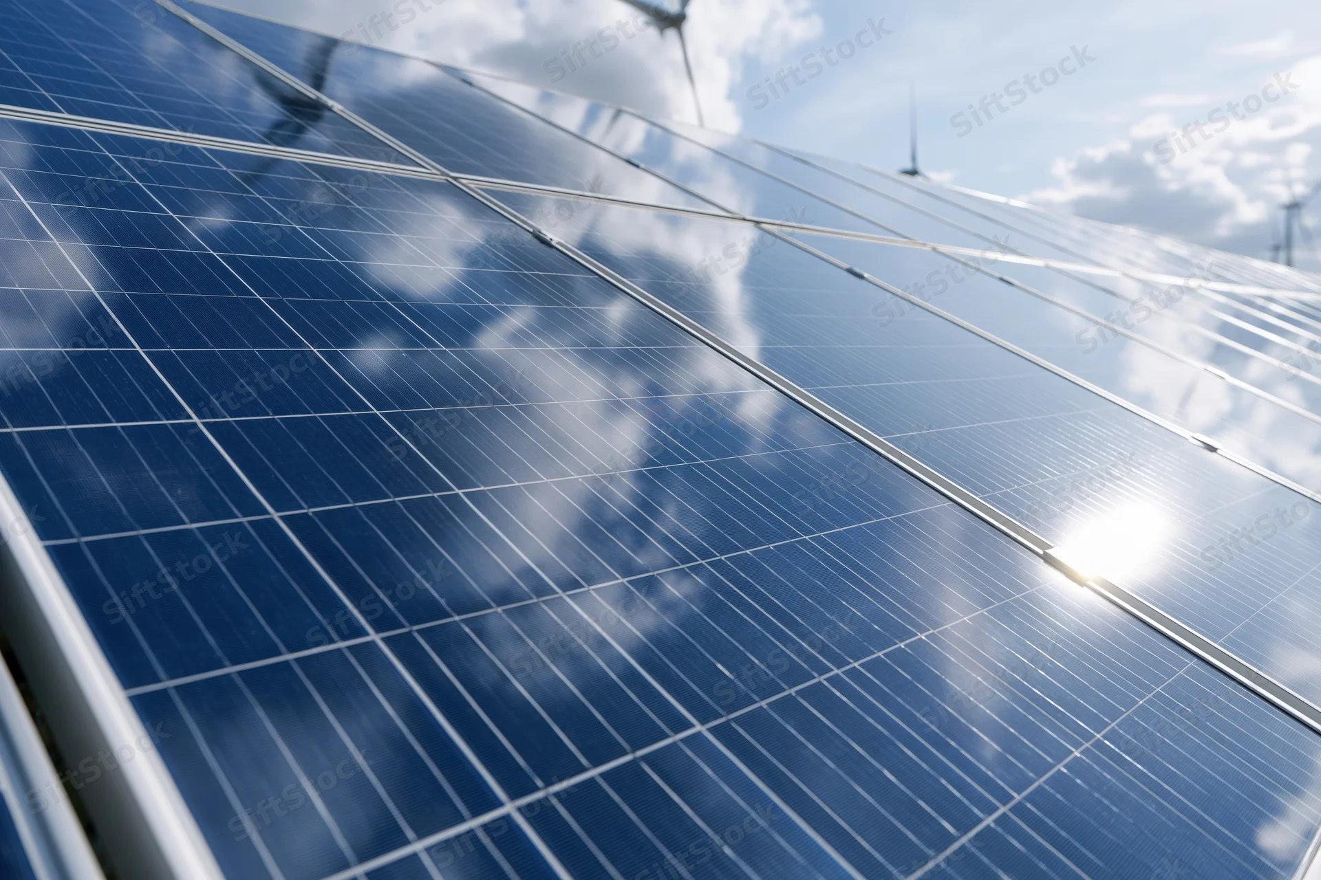 Close-up low-angle view of large solar panels under bright sky with clouds reflected on surface