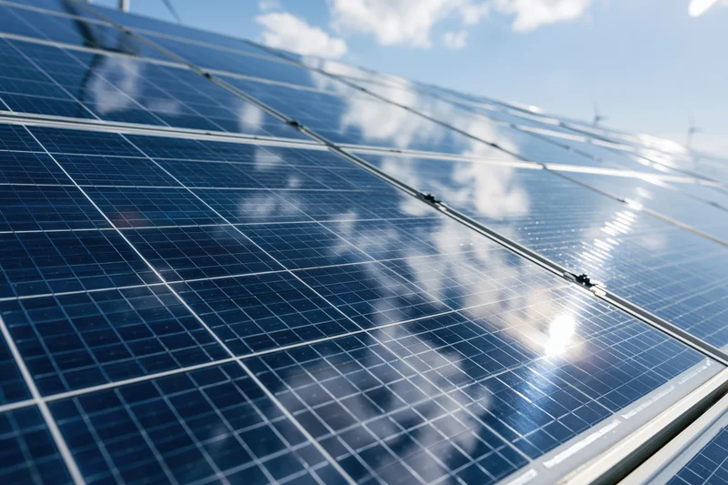 Close-up low-angle view of large solar panels reflecting sky and clouds under bright daylight