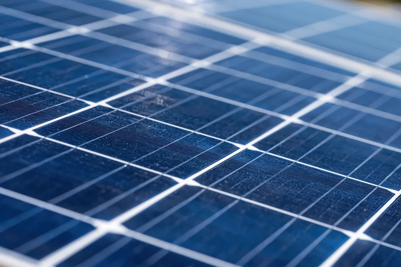 Close-up of solar panel surface showing blue photovoltaic cells and white gridlines under sunlight