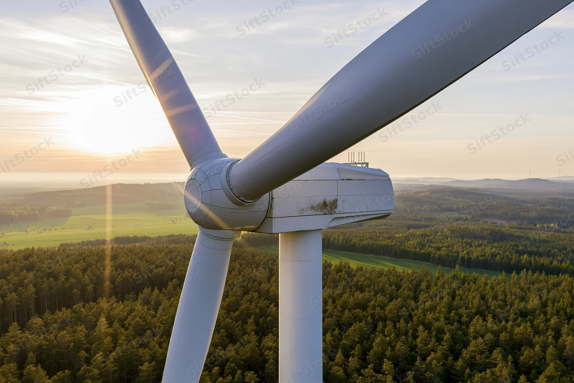 Close aerial view of wind turbine hub and three blades over forested landscape at sunset