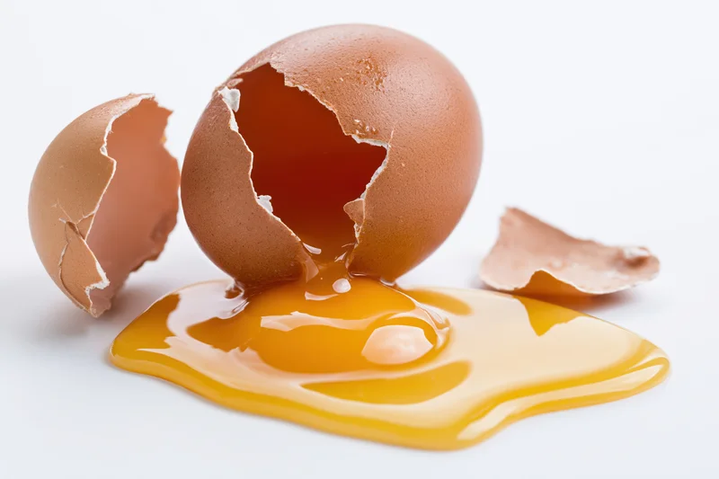 Cracked brown egg broken open on white surface with yolk spilled