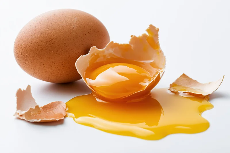 Cracked brown egg broken open on white surface with yolk spilled