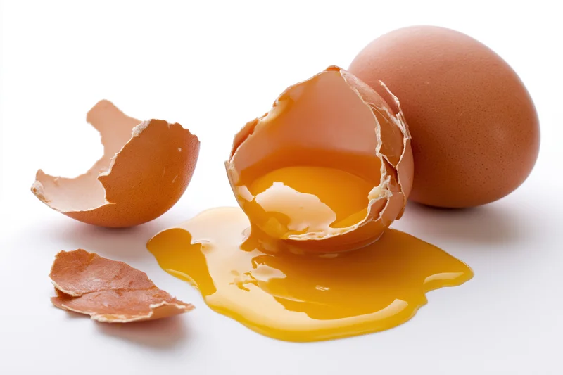 Cracked brown egg broken open on white surface with yolk spilled