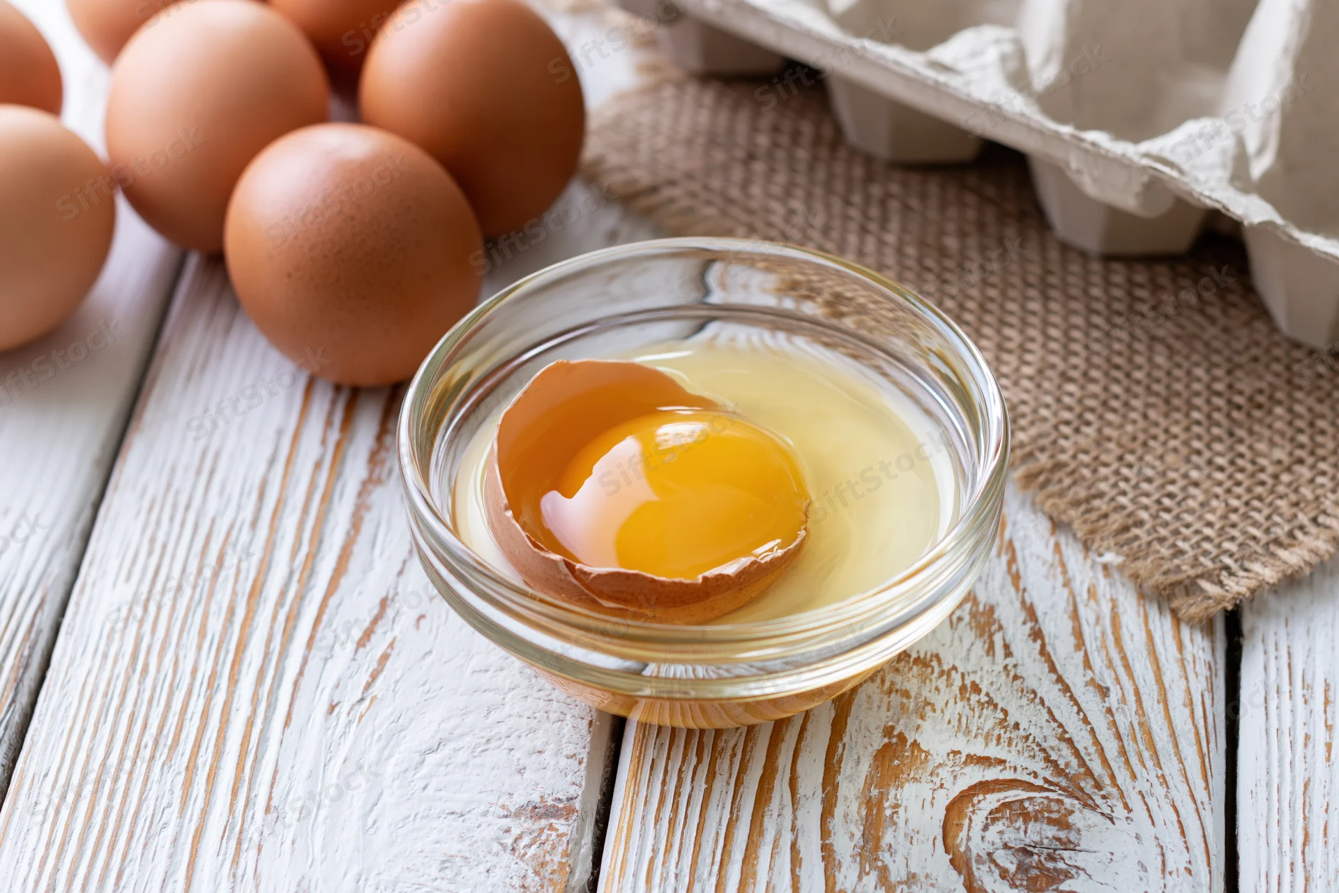 Cracked brown egg with yolk in a small glass bowl on a rustic wooden table