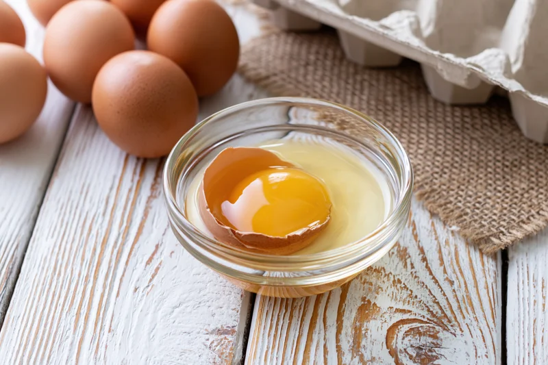 Cracked brown egg with yolk in a small glass bowl on a rustic wooden table