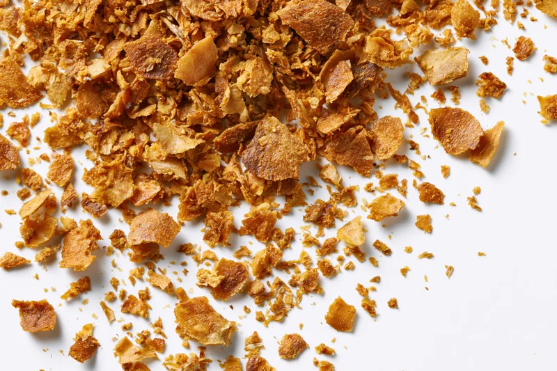 Dried brown herb flakes and spice fragments scattered on white surface