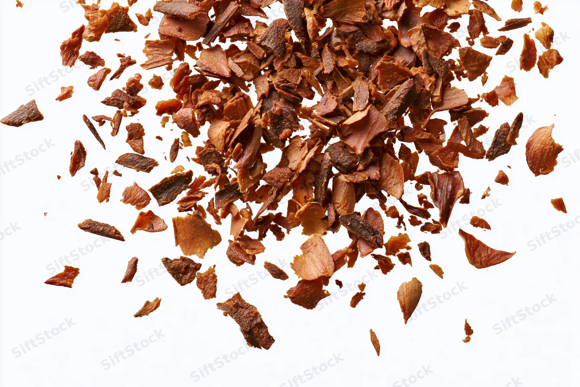Dried brown herb flakes and spice fragments scattered on white background