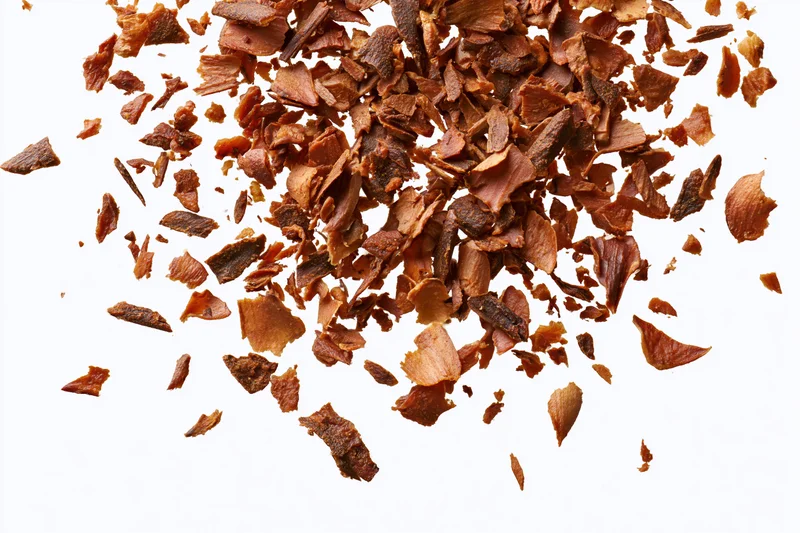 Dried brown herb flakes and spice fragments scattered on white background