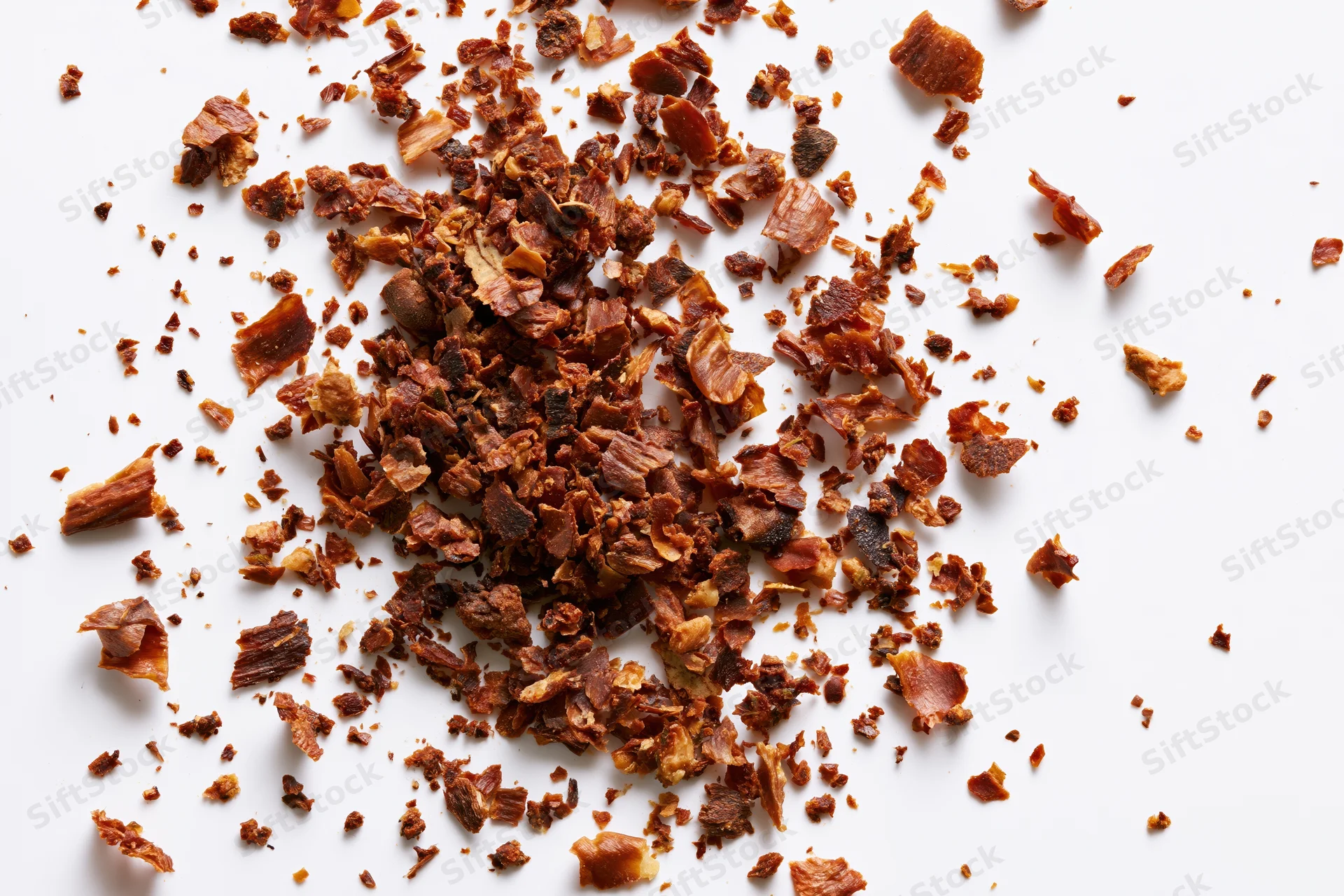 Dried brown herb flakes and spice fragments scattered on white background