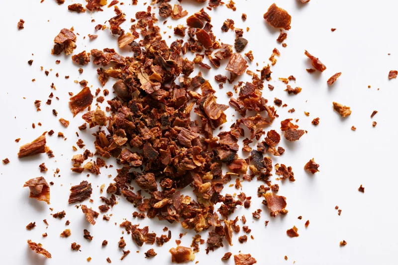Dried brown herb flakes and spice fragments scattered on white background