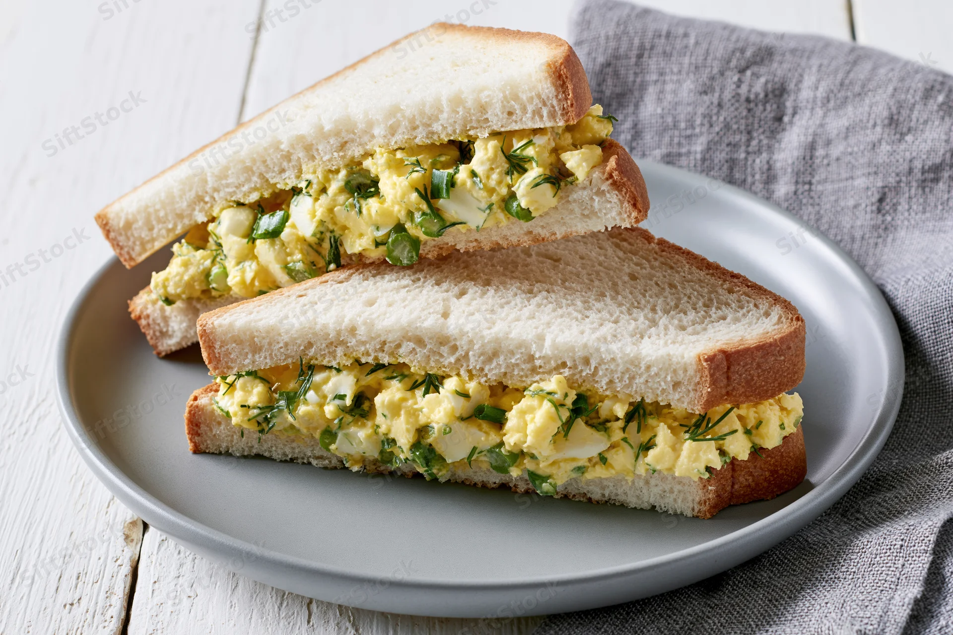 Egg salad sandwich cut into two triangles on a round grey ceramic plate