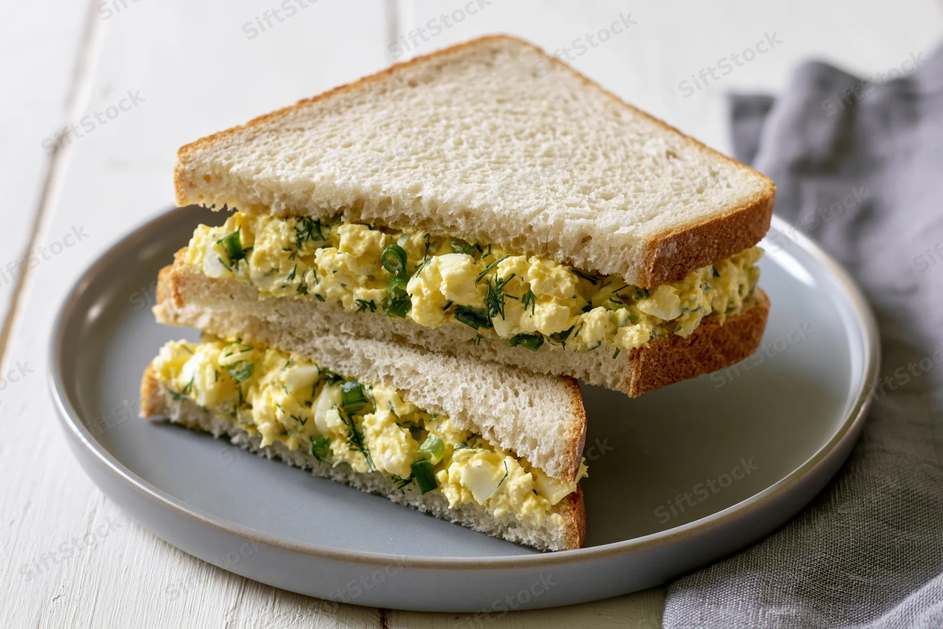 Egg salad sandwich cut into two triangles stacked on a round gray plate on a wooden surface