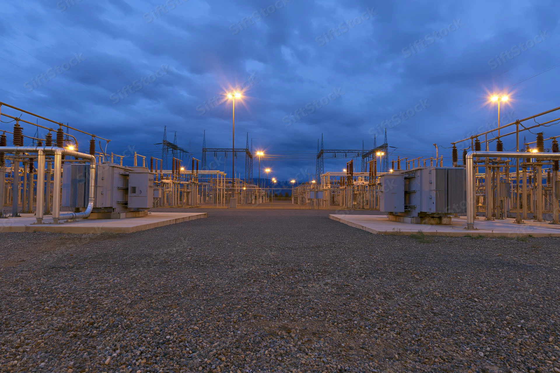 Rows of high-voltage transformers and electrical equipment in an outdoor substation at dusk