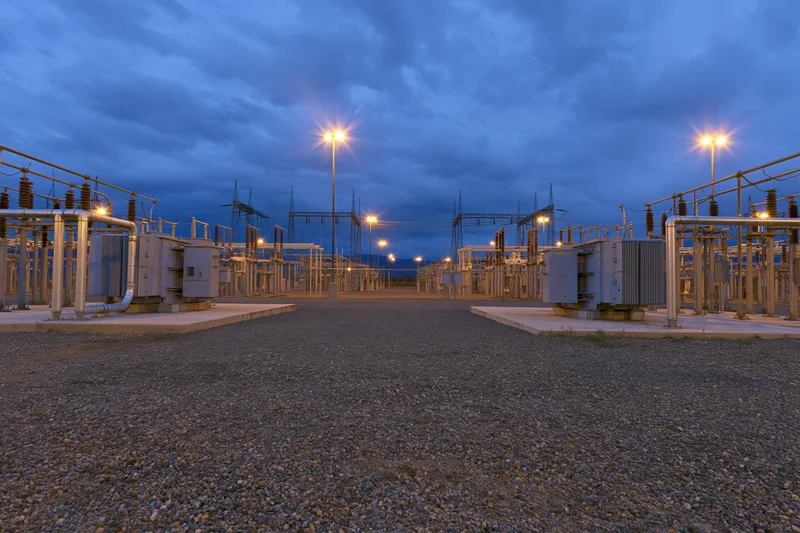 Rows of high-voltage transformers and electrical equipment in an outdoor substation at dusk