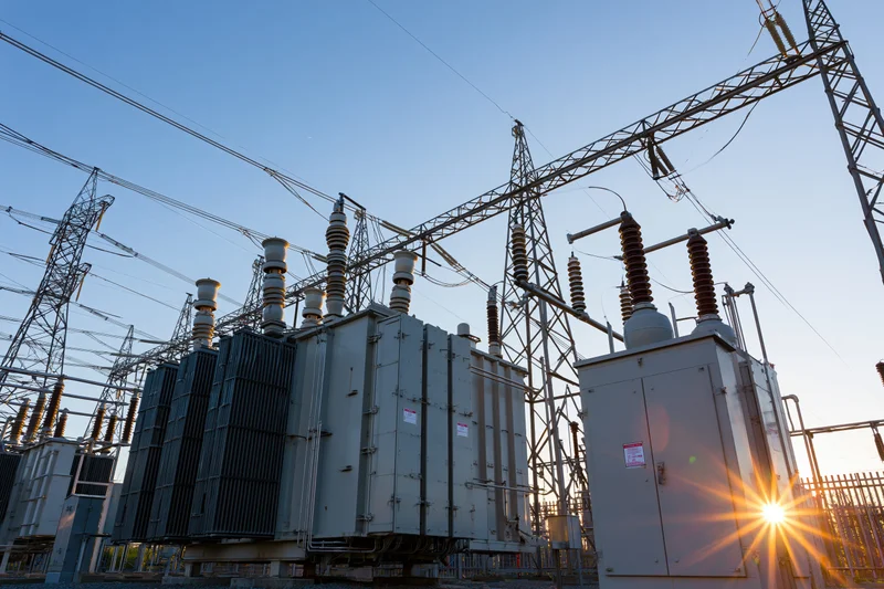 Electrical substation with transformers and transmission towers under clear blue sky at sunrise