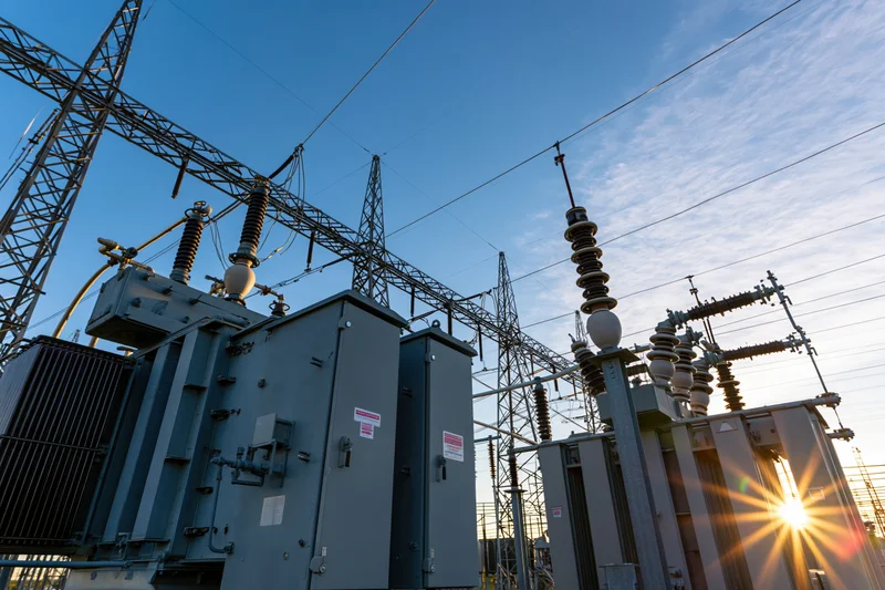 Electrical substation with transformers and transmission towers viewed from ground level at dusk