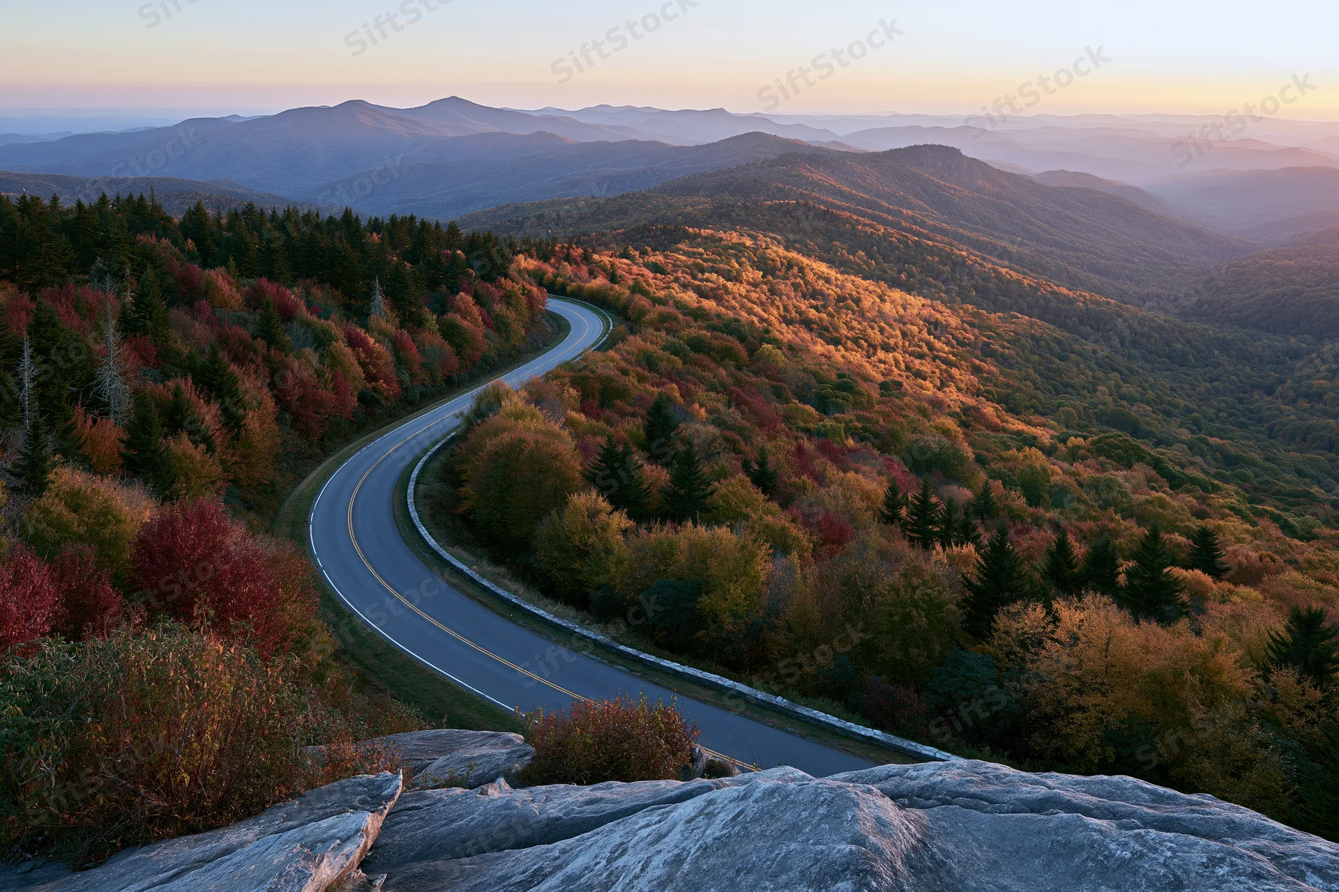 Winding two-lane road through autumn forest on mountain ridge at sunset
