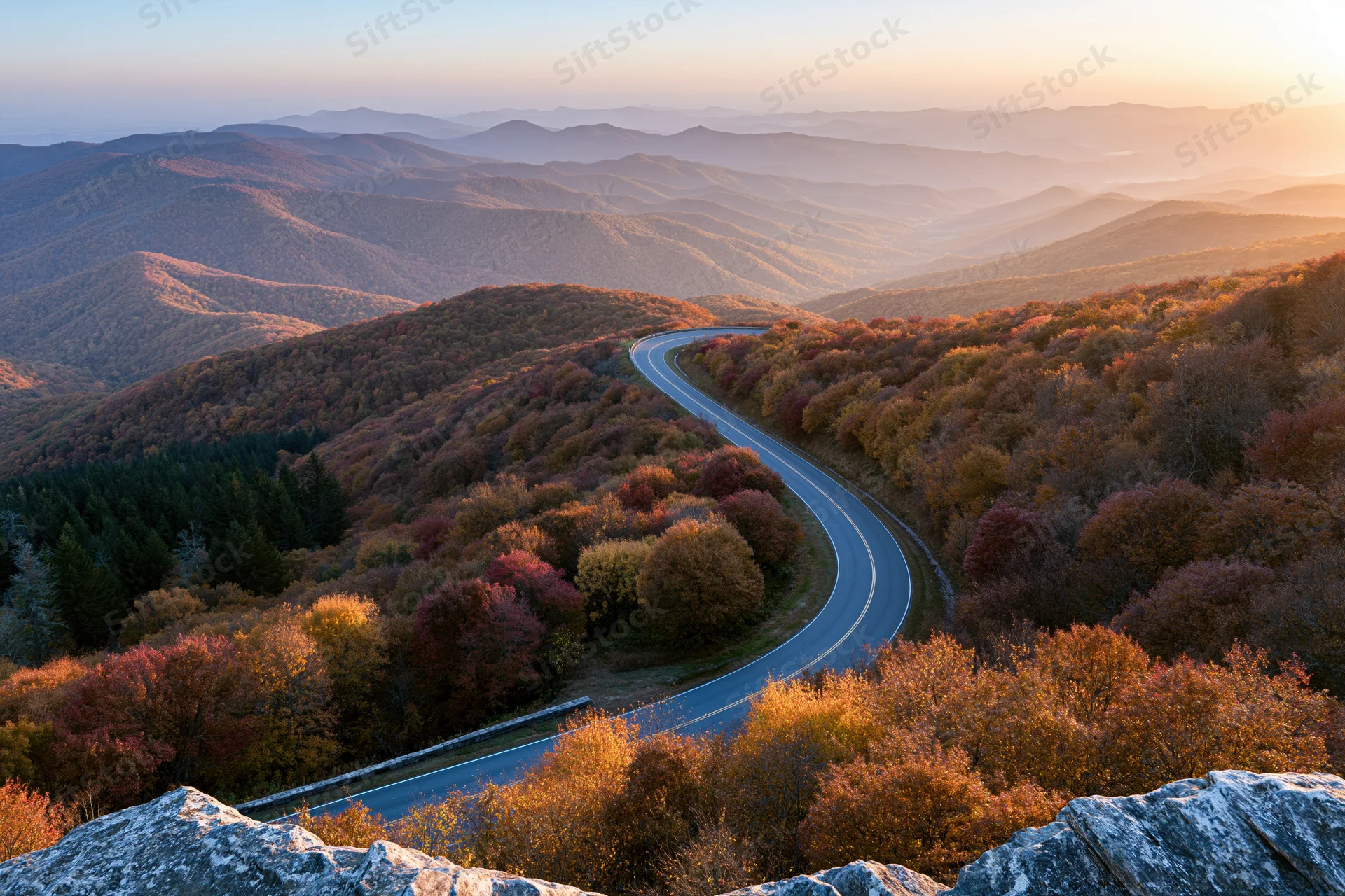 Winding two-lane mountain highway through autumn forest at sunset elevation view
