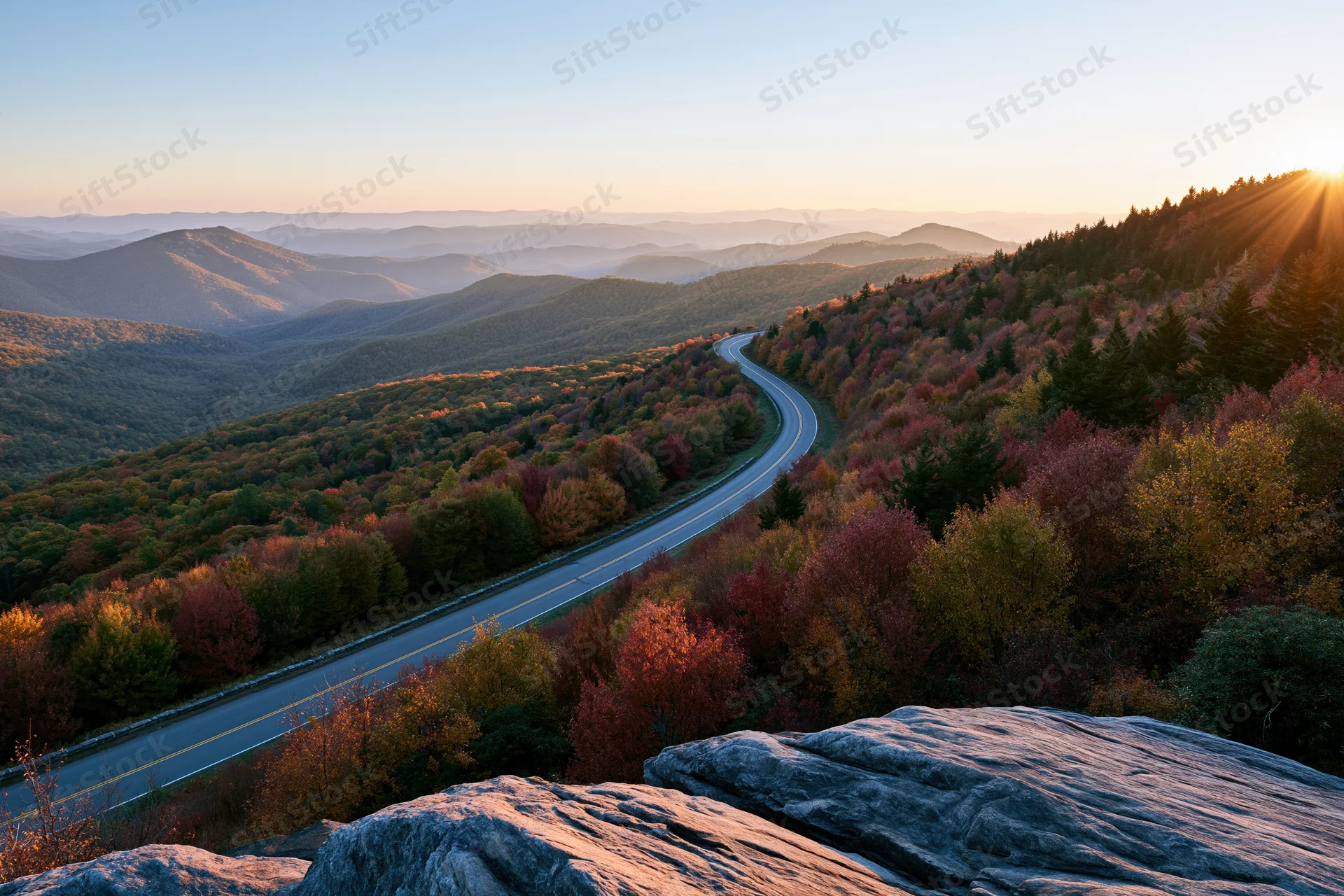 Winding two-lane highway through autumn forested mountains at sunset from elevated overlook
