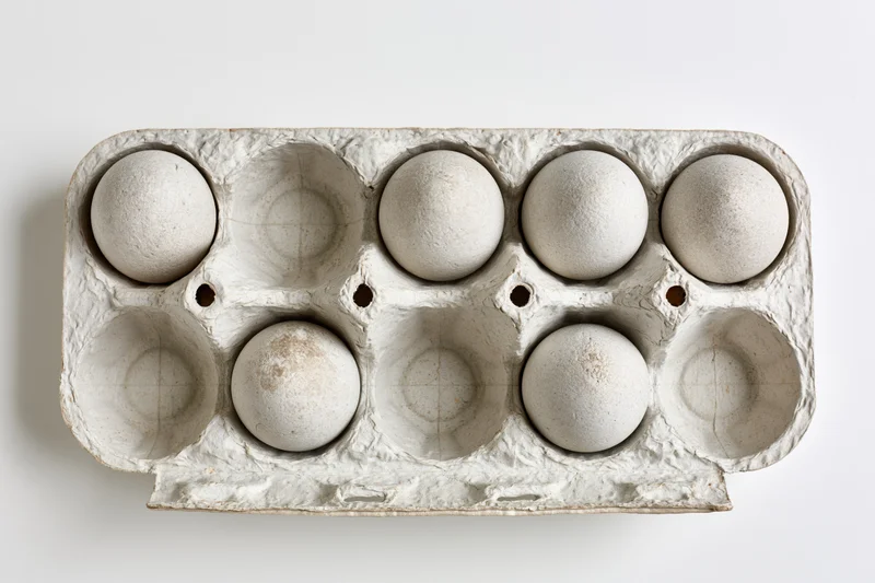 Open recycled cardboard egg carton with six white eggs arranged in two rows on plain white background