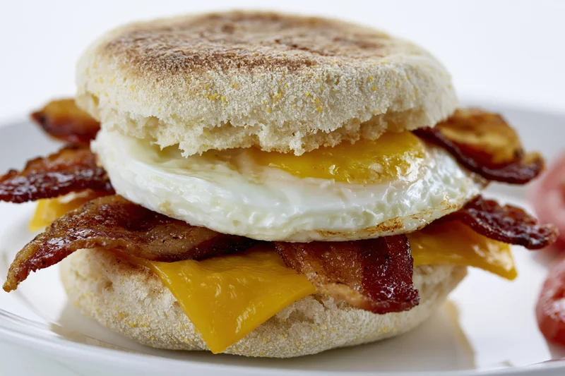 English muffin breakfast sandwich with fried egg and crispy bacon on a white plate