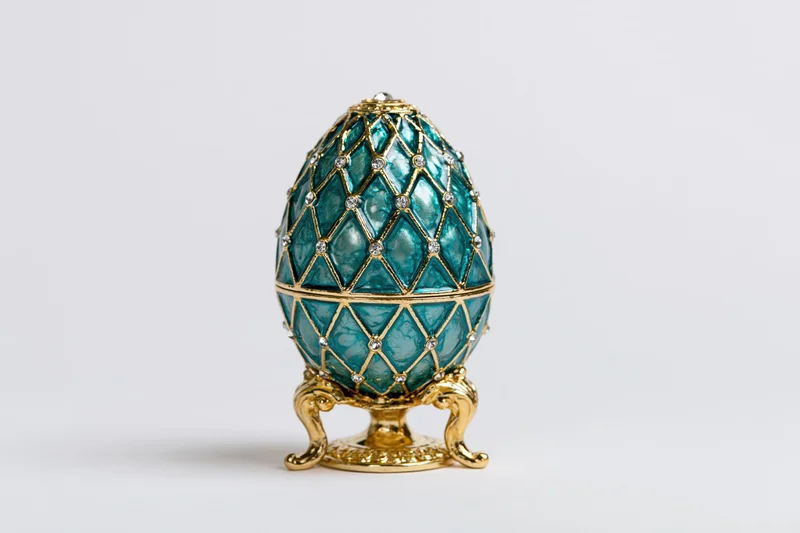 Teal enamel decorative egg with gold lattice and gemstones on a gilded stand