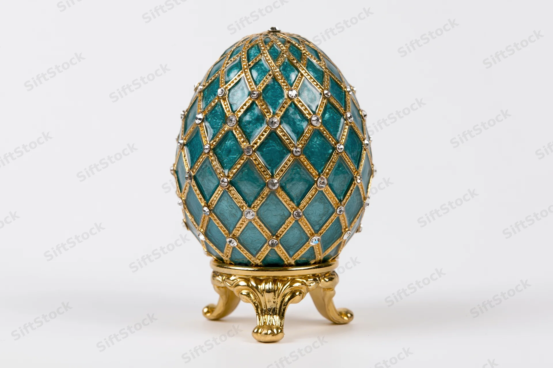 Teal enamel decorative egg with gold lattice and gemstones on a golden stand