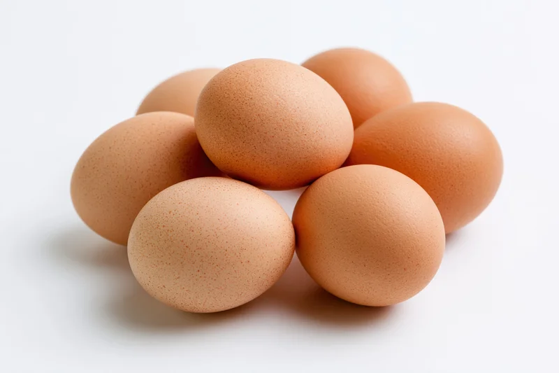 Brown chicken eggs grouped together in a loose cluster on a white surface