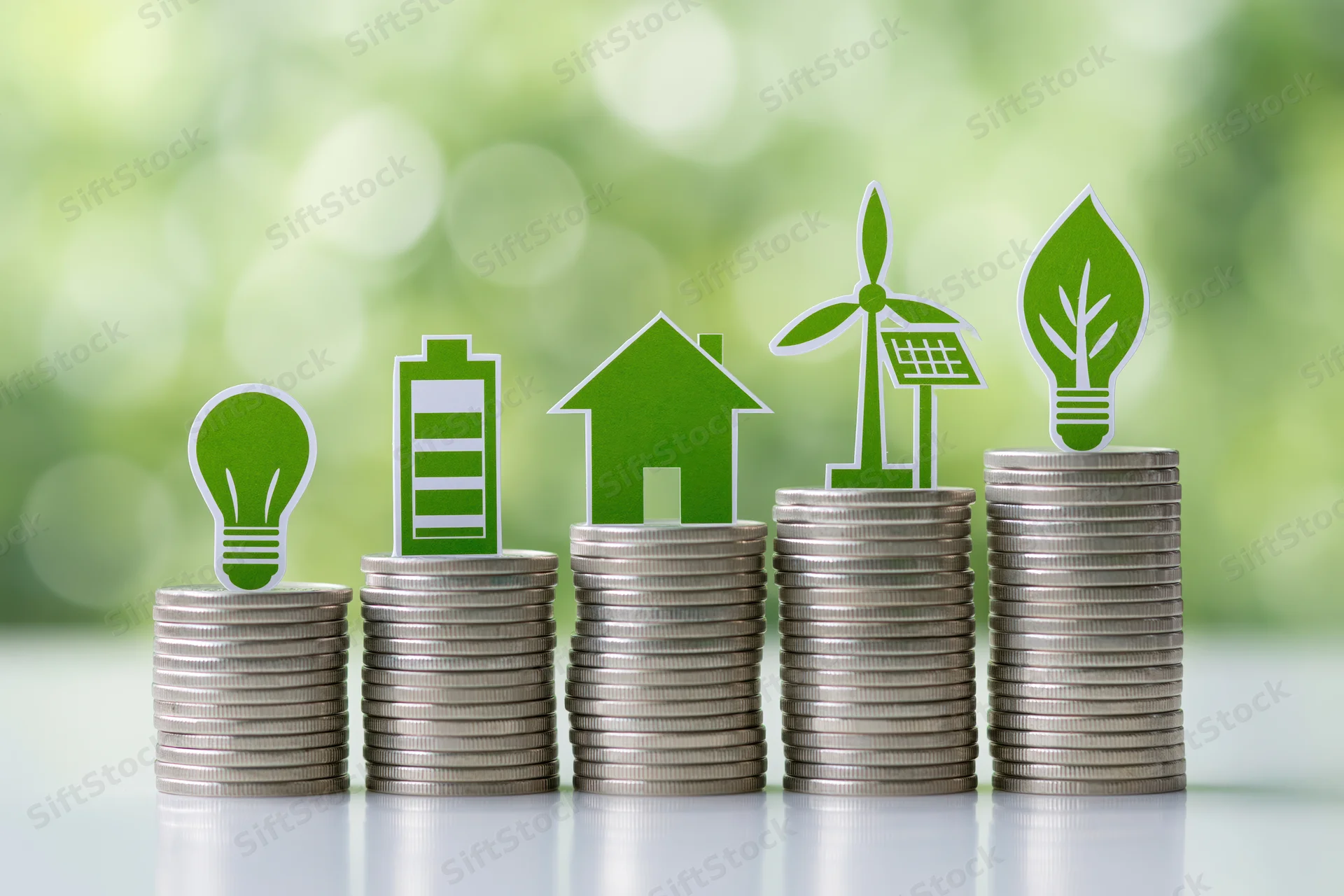 Five stacks of silver coins arranged in ascending height with green eco icons on top against a blurred green background
