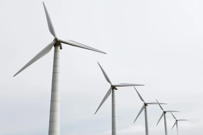 Wind turbines arranged in diagonal row receding into overcast sky