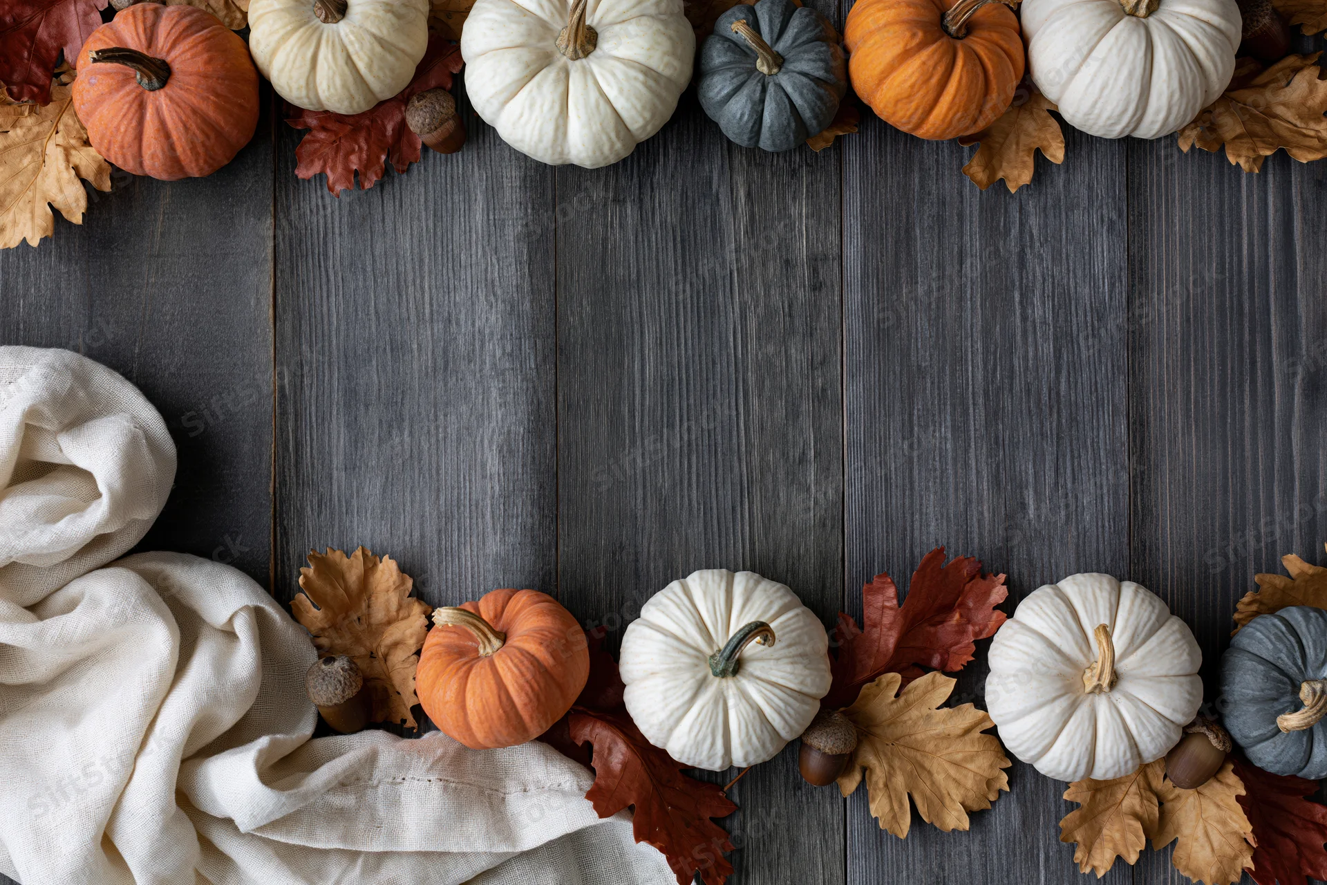 Small decorative pumpkins and dried oak leaves arranged in a border on a dark wooden table with copyspace in the center