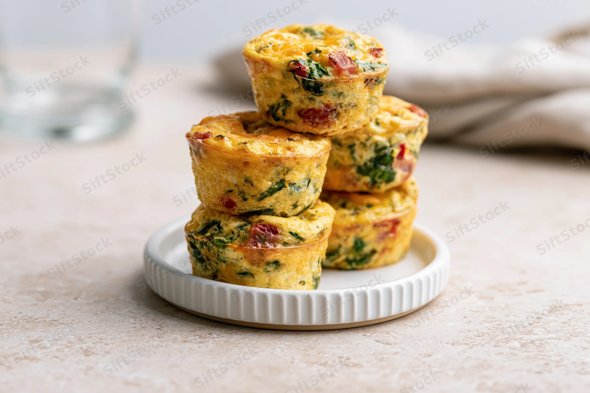 Egg muffin cups stacked on a small white ridged plate on a beige countertop