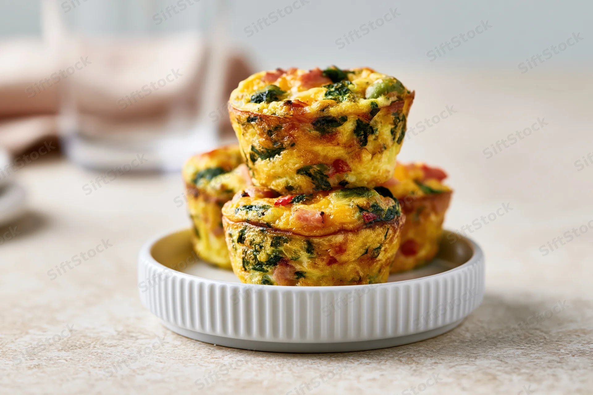 Golden-brown egg muffin cups stacked on a small white ridged plate on a kitchen table