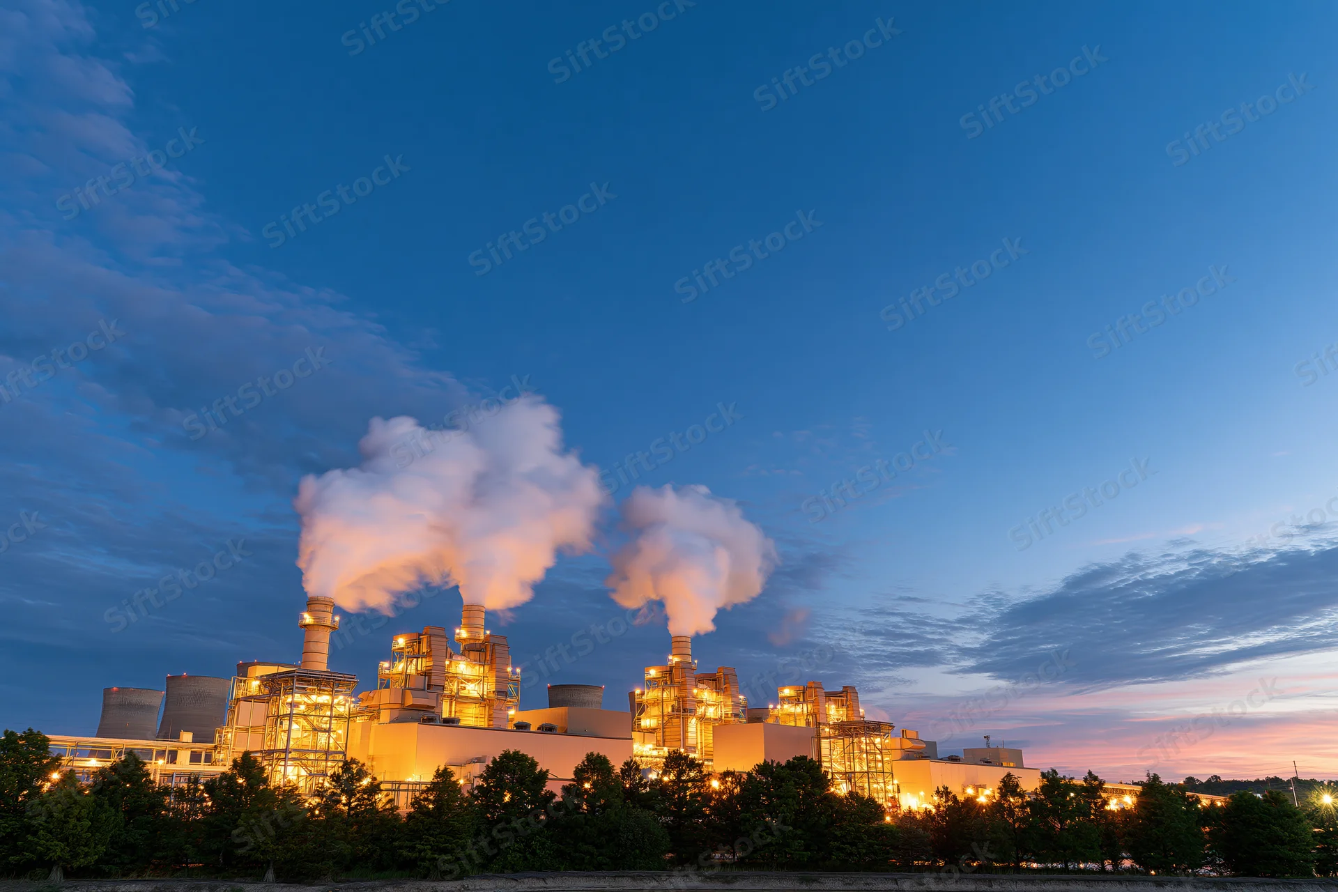 Gas turbine power plant glowing with warm amber lights at dusk against a blue sky with steam rising from smokestacks