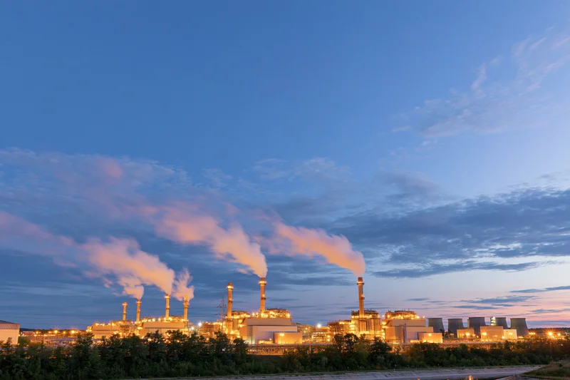 Gas turbine power plant emitting steam from smokestacks at dusk with warm artificial lighting