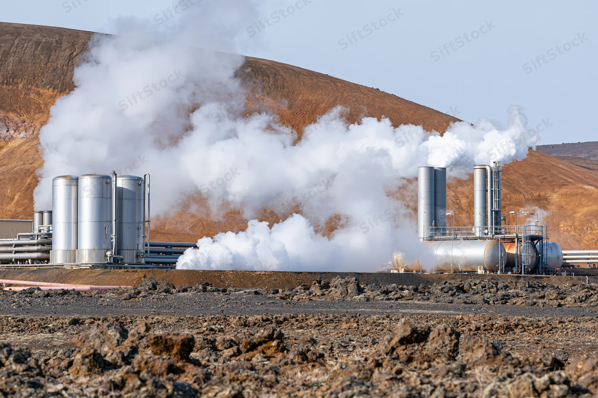 Geothermal power plant releasing steam from metal tanks and stacks in arid landscape