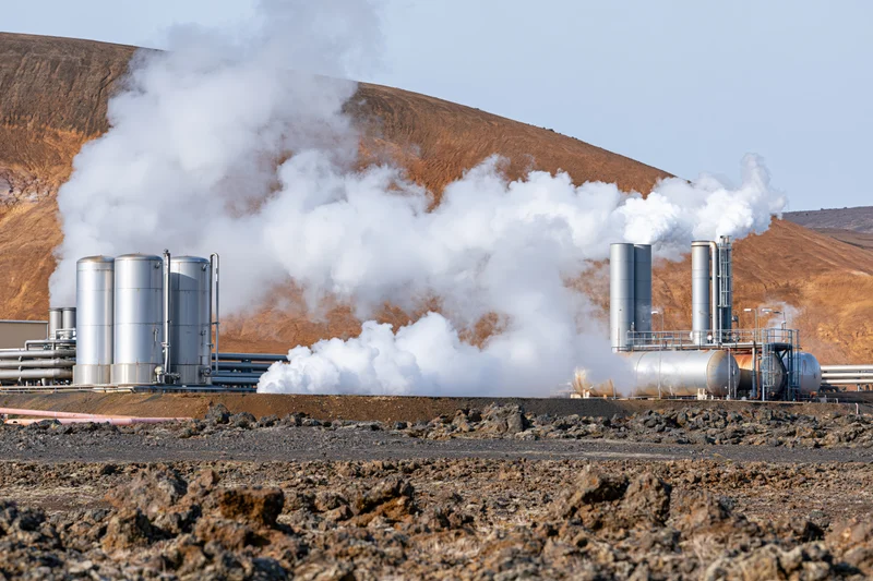 Geothermal power plant releasing steam from metal tanks and stacks in arid landscape
