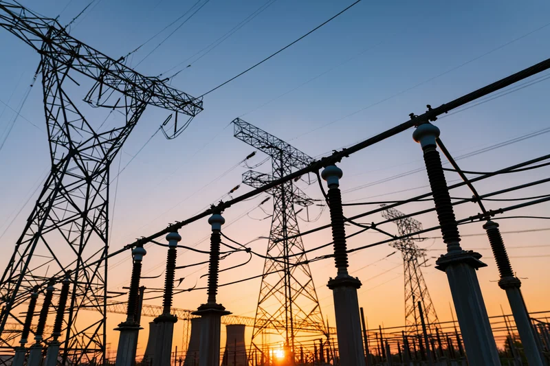 High-voltage electrical substation equipment silhouetted against a dusky sky with transmission towers and insulators in the foreground