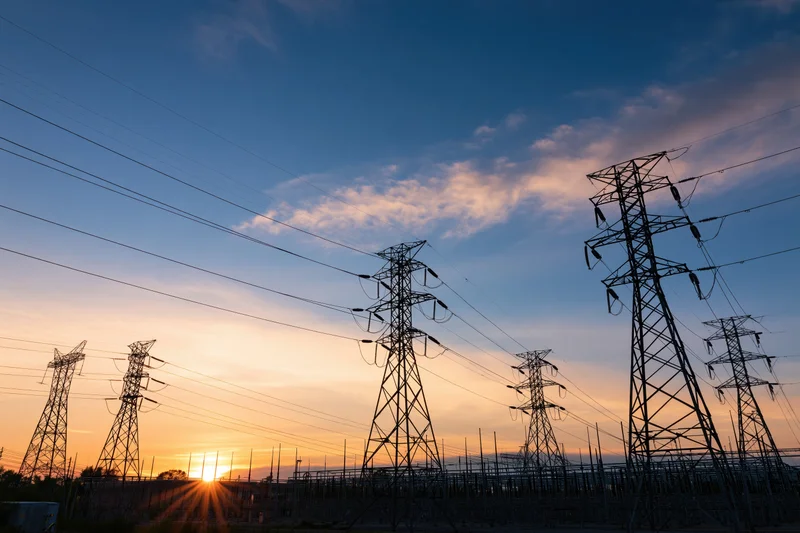 High-voltage transmission towers silhouetted against a sunset sky at an electrical substation