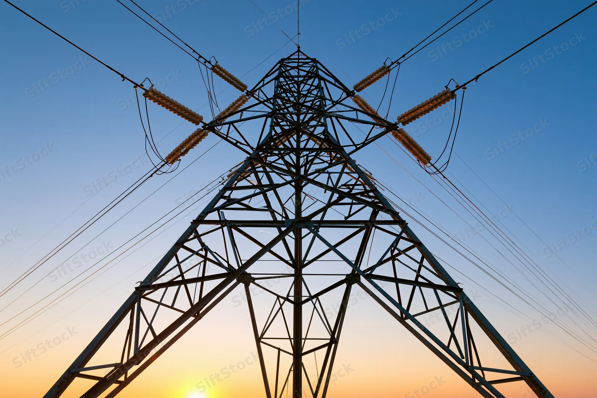High-voltage electricity transmission tower silhouetted against a sunset sky