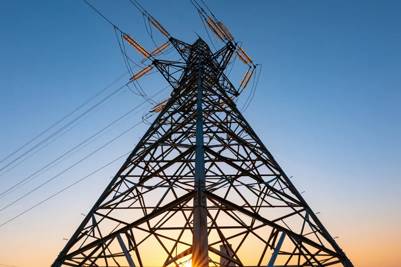 High-voltage electricity transmission tower viewed from below against a sunset sky