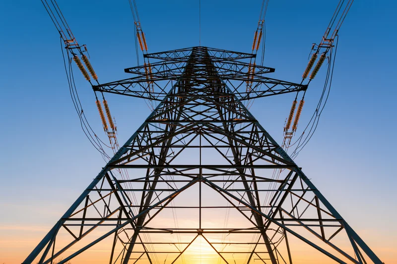 High-voltage electricity transmission tower viewed from below against a sunset sky