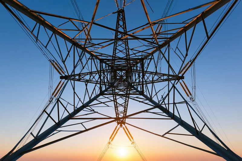 High-voltage electricity transmission tower viewed from below against sunset sky