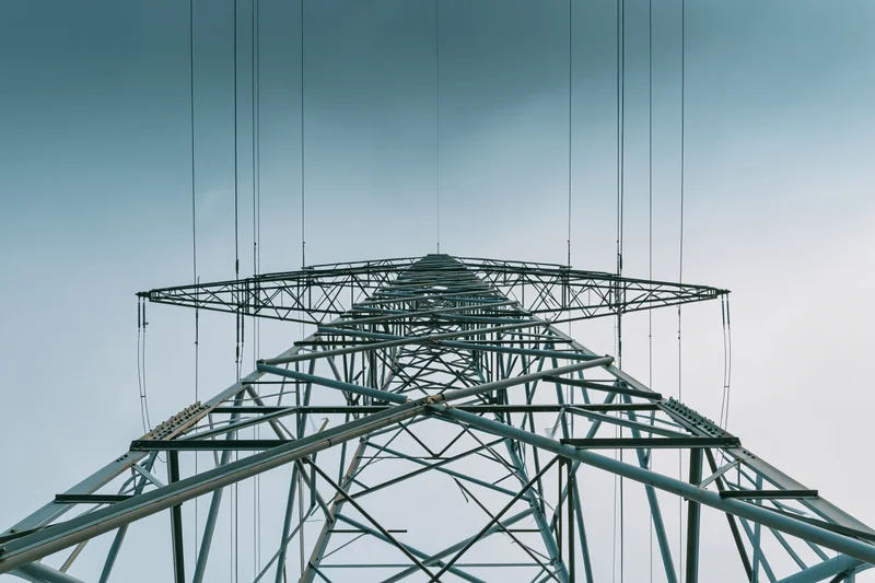 High-voltage steel electricity transmission pylon viewed from below against a clear blue sky