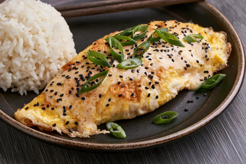 Pan-fried egg omelet with rice on a dark plate, garnished with sesame seeds and green onions