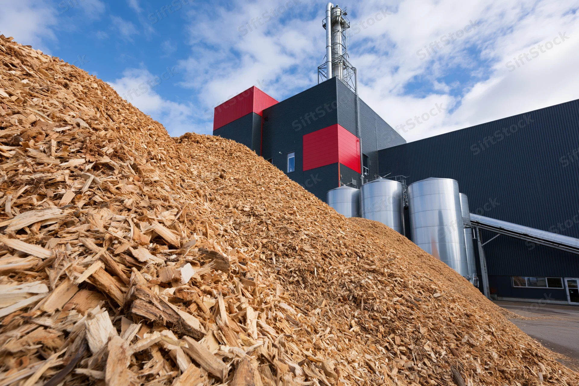 Large mound of wood chip biomass fuel in front of industrial energy plant