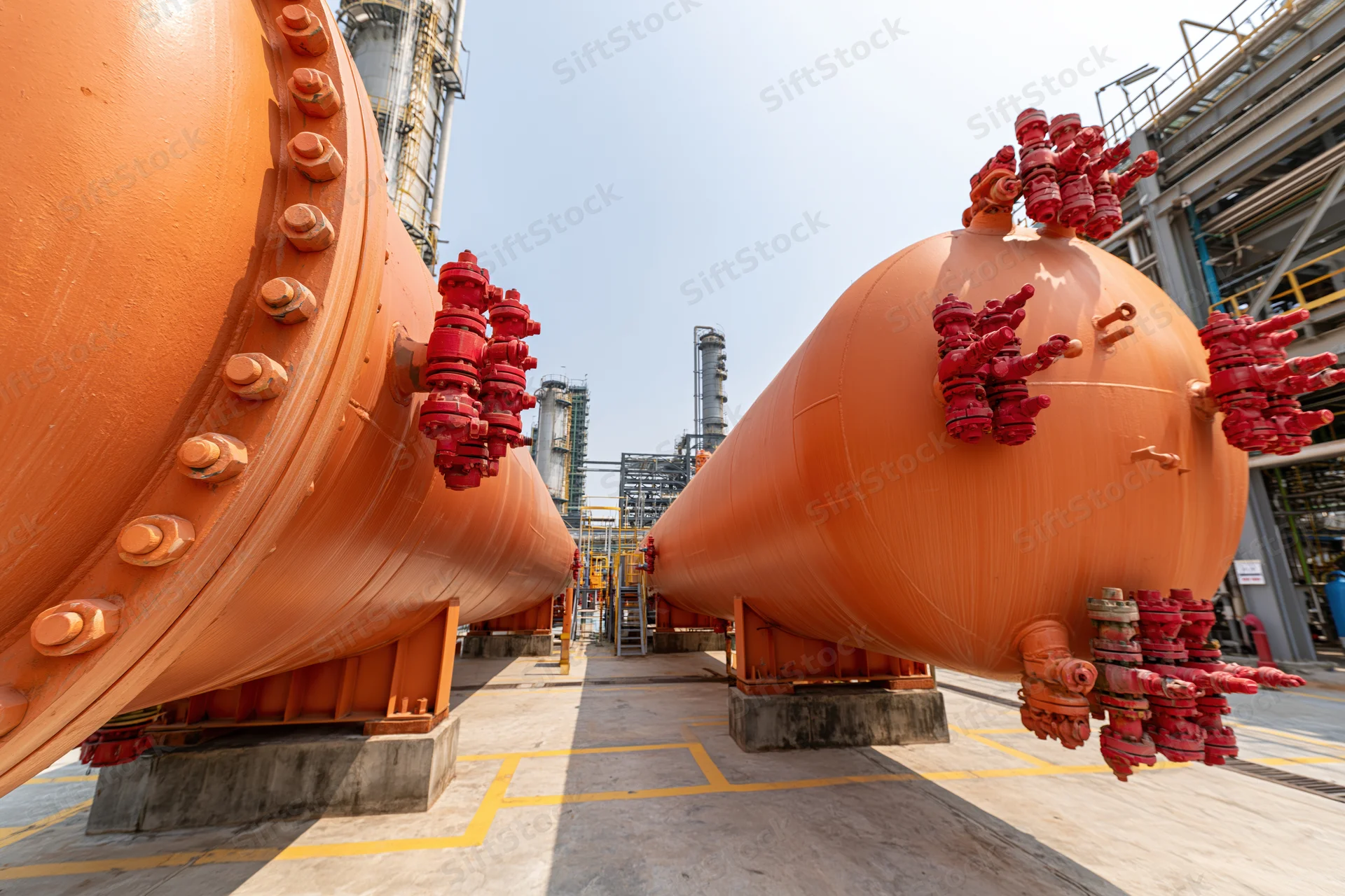 Large orange cylindrical pressure vessels with red valve clusters arranged in a refinery plant setting