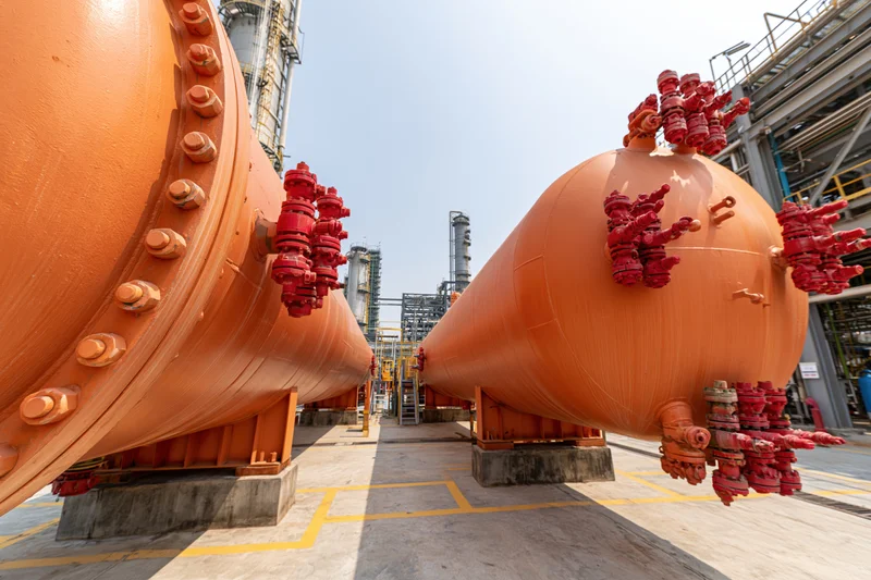 Large orange cylindrical pressure vessels with red valve clusters arranged in a refinery plant setting