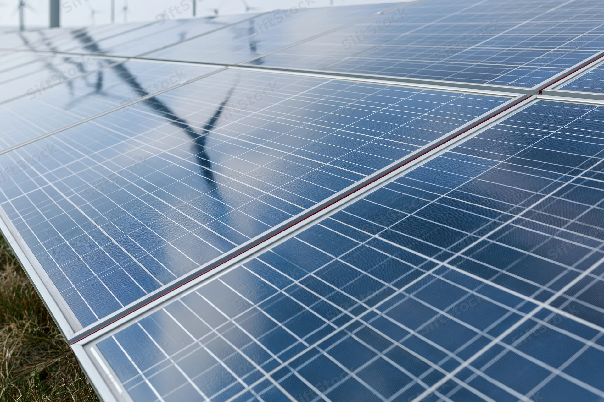 Solar panels arranged in a large outdoor array with wind turbines visible in the background